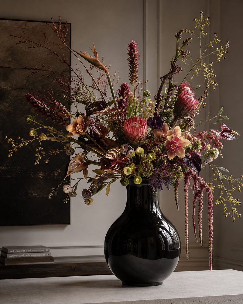 Stillleben aus schwarzer Keramikvase und wildem Blumenflor vor dunkler Wand